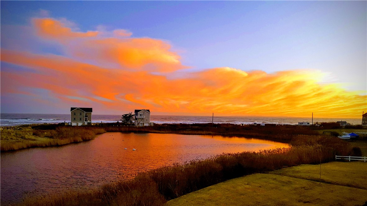Coastal pond and ocean at sunset, with beach grasses and houses along the shore.