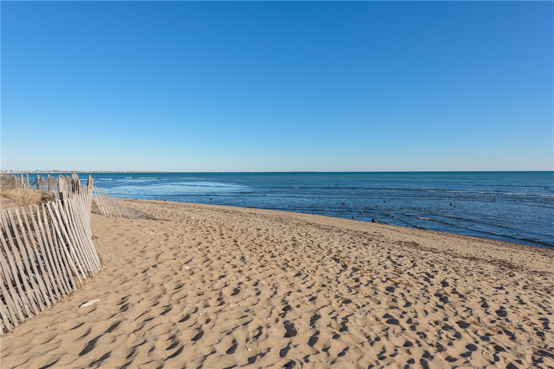 Sandy beach beside calm blue water, with a weathered wooden fence along the shore.