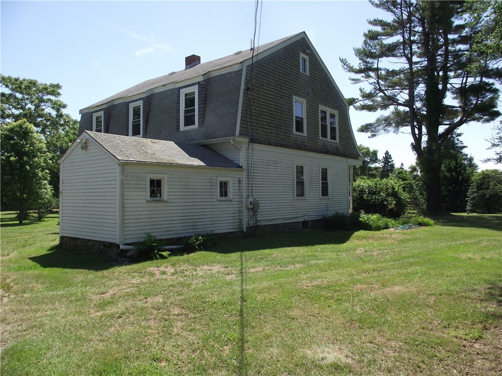 Two-story house with white siding and a dark gambrel roof, viewed from the side across a lawn.