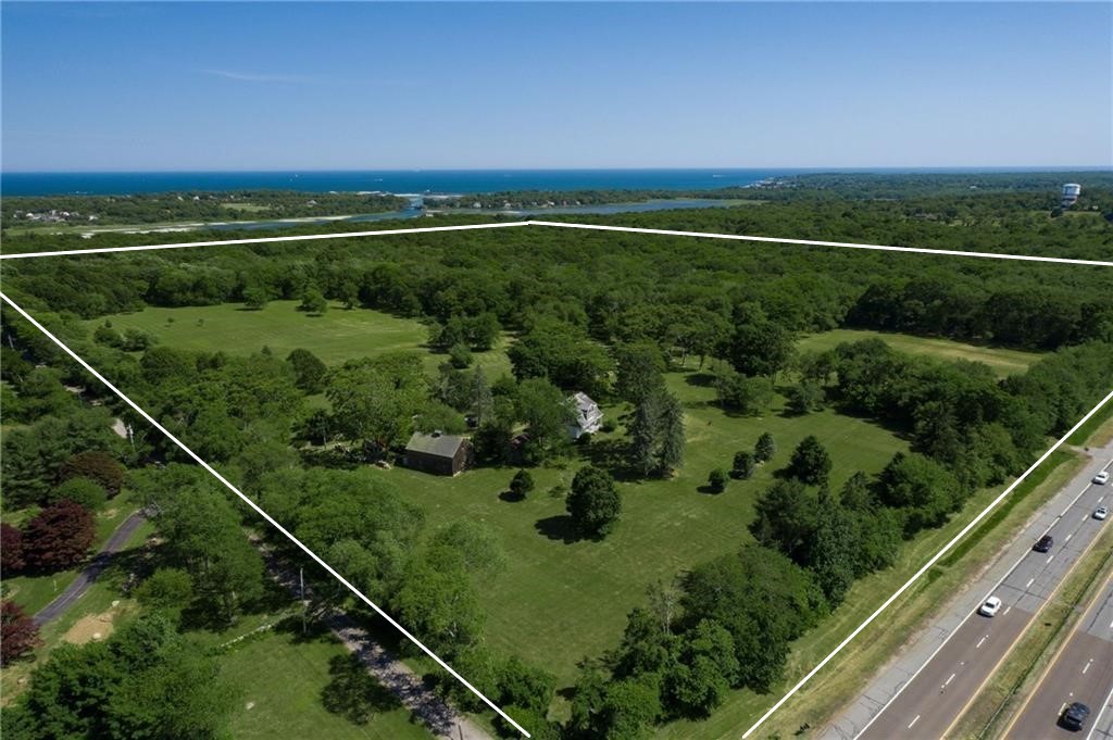 Aerial view of wooded property with open lawns, a house, and the ocean in the distance.