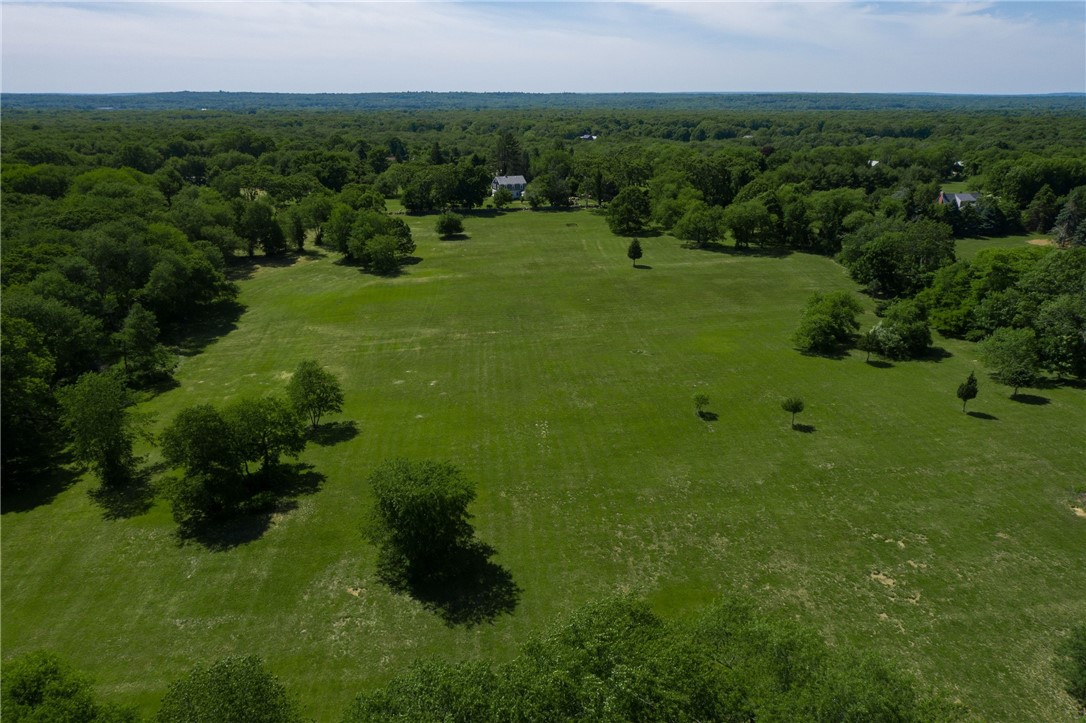 Aerial view of a broad grassy field dotted with trees and bordered by woodland.