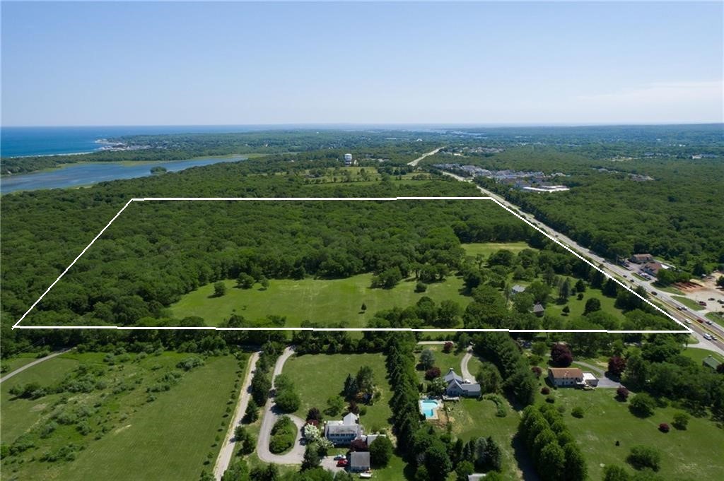 Outlined wooded parcel with open grass, neighboring homes, and water in the distance.