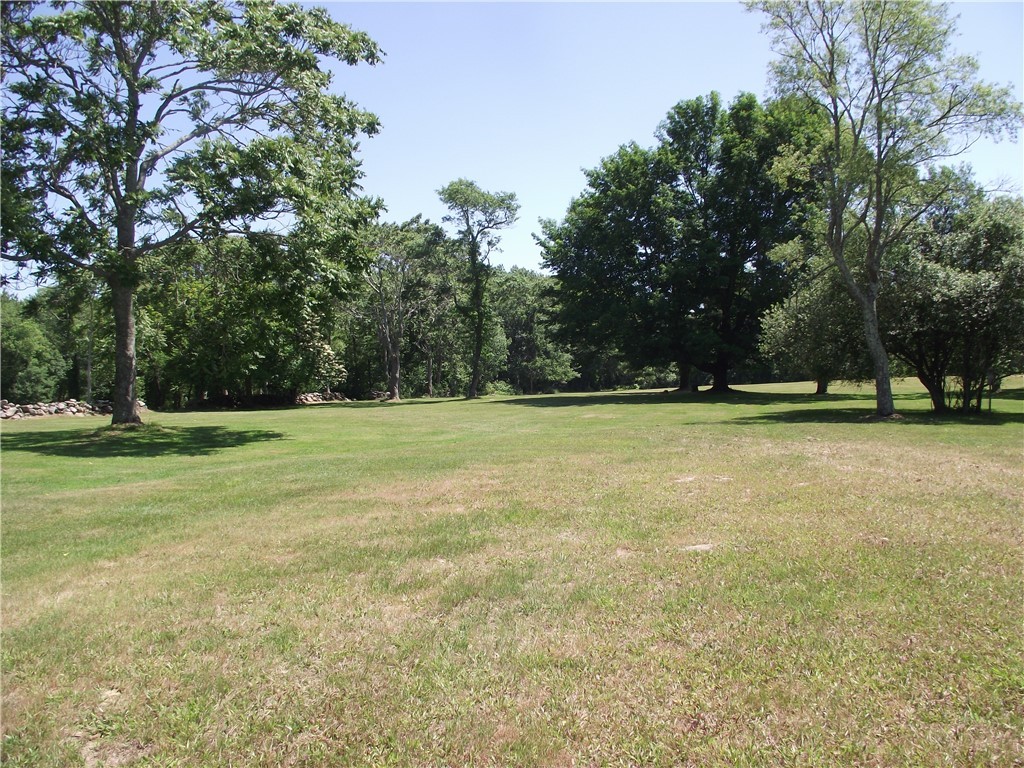 Broad grassy lawn bordered by mature trees and a low stone wall.