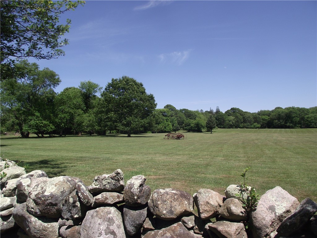 Grassy field with mature trees and old farm equipment beyond a low stone wall.