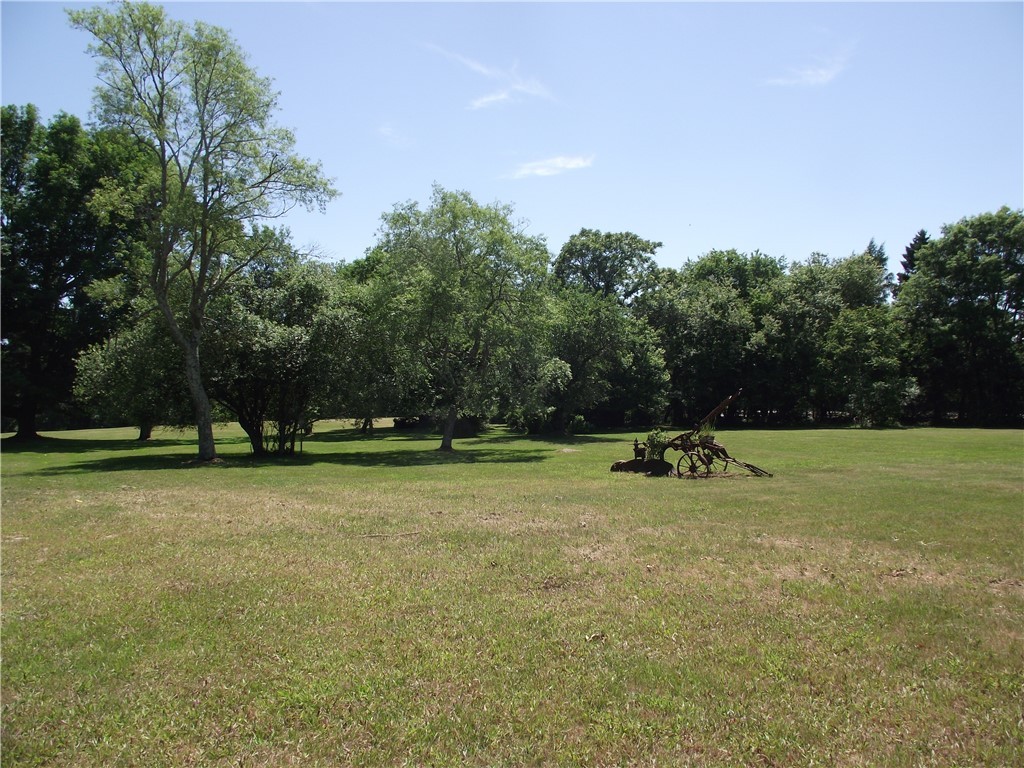 Grassy property grounds bordered by mature trees, with antique farm equipment in the open lawn.