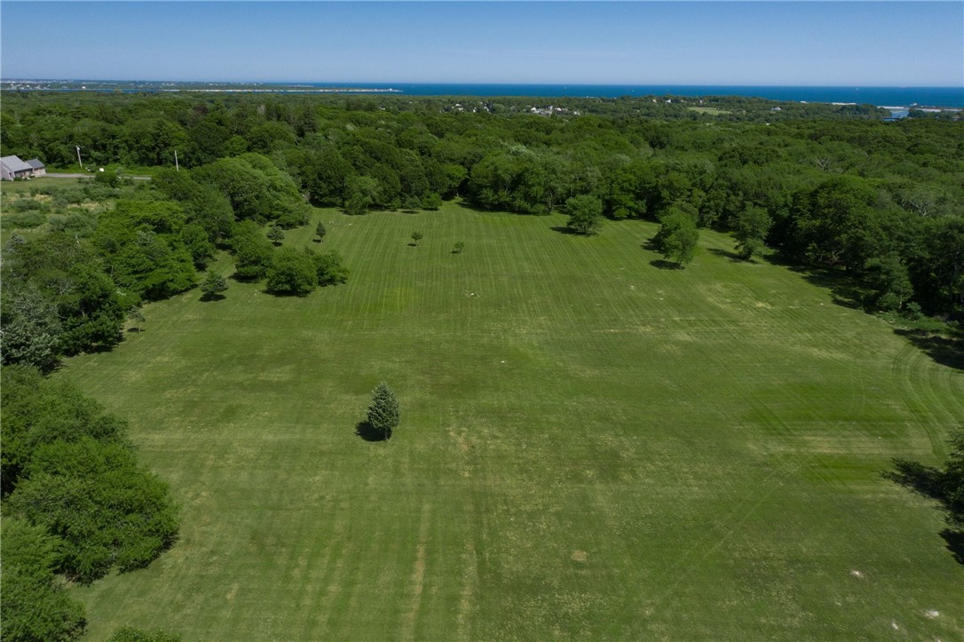 Aerial view of a broad mowed clearing bordered by trees, ocean on the horizon.