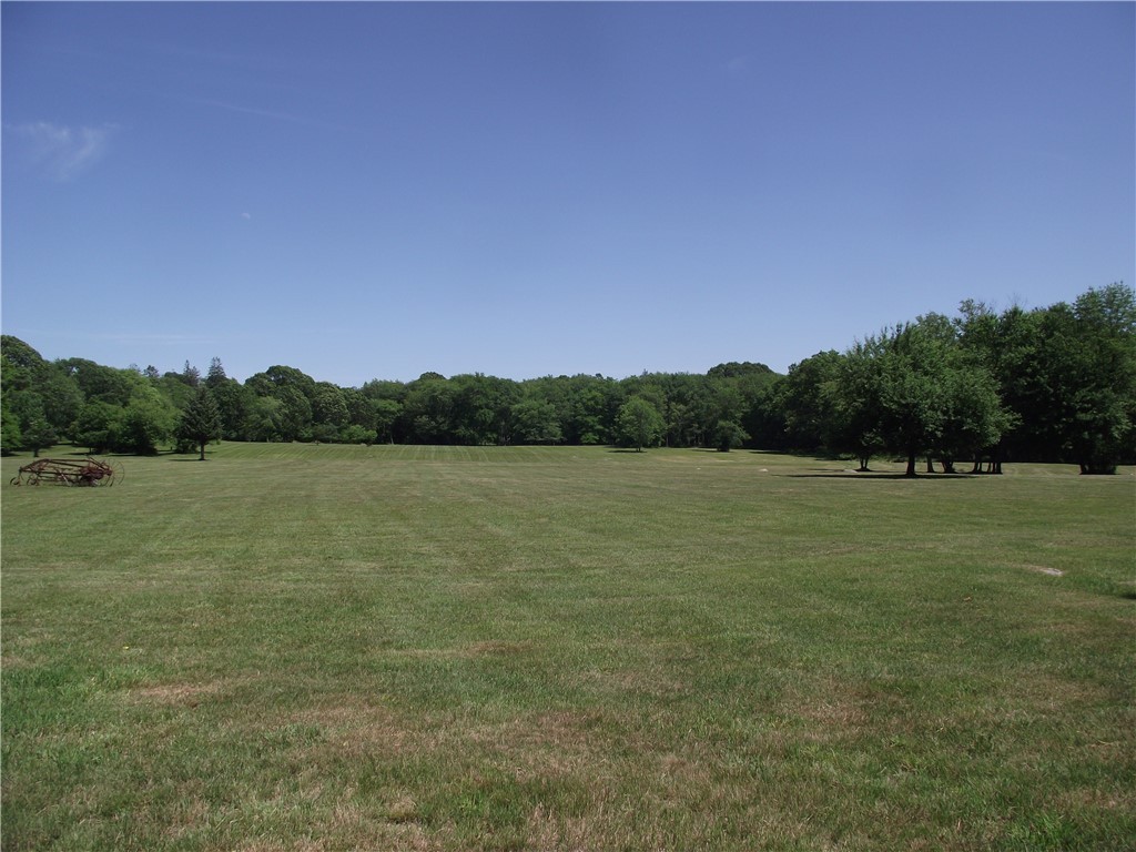 Open grassy field bordered by mature trees, with old farm equipment at the left edge.