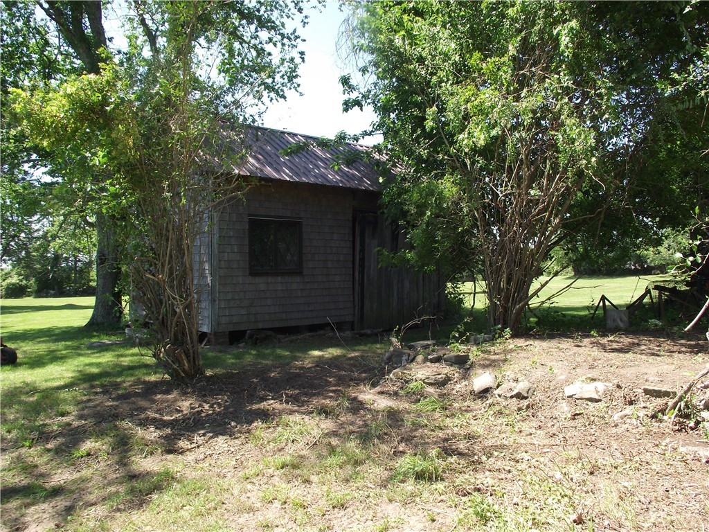 Small shingle-sided outbuilding with a metal roof tucked among trees beside a lawn.