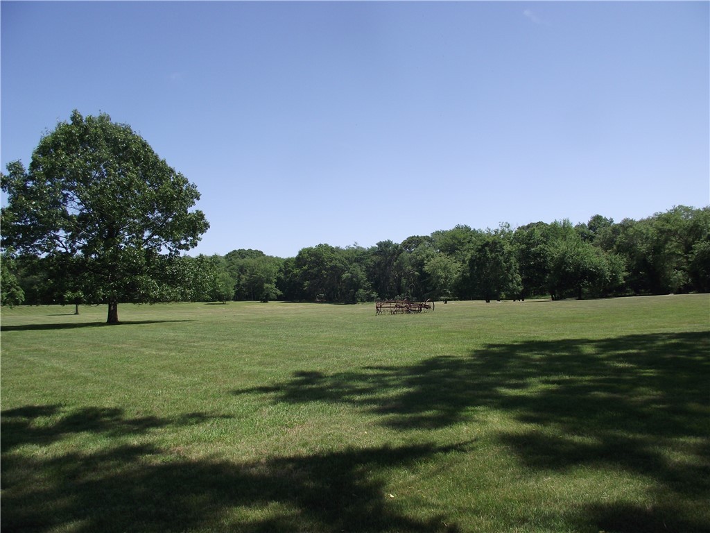 Expansive mown lawn with a mature shade tree and antique farm equipment in the distance.