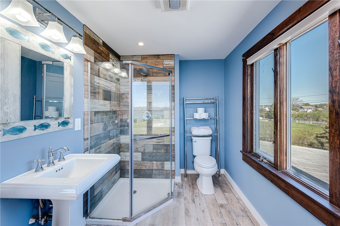 Bathroom with a glass-enclosed wood-look tile shower, blue walls, and large dark-framed windows.