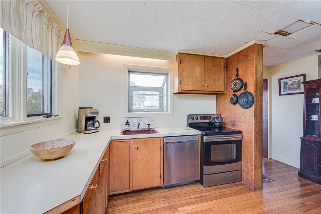 Kitchen with wood cabinets, white counters, stainless steel dishwasher, and hardwood flooring.
