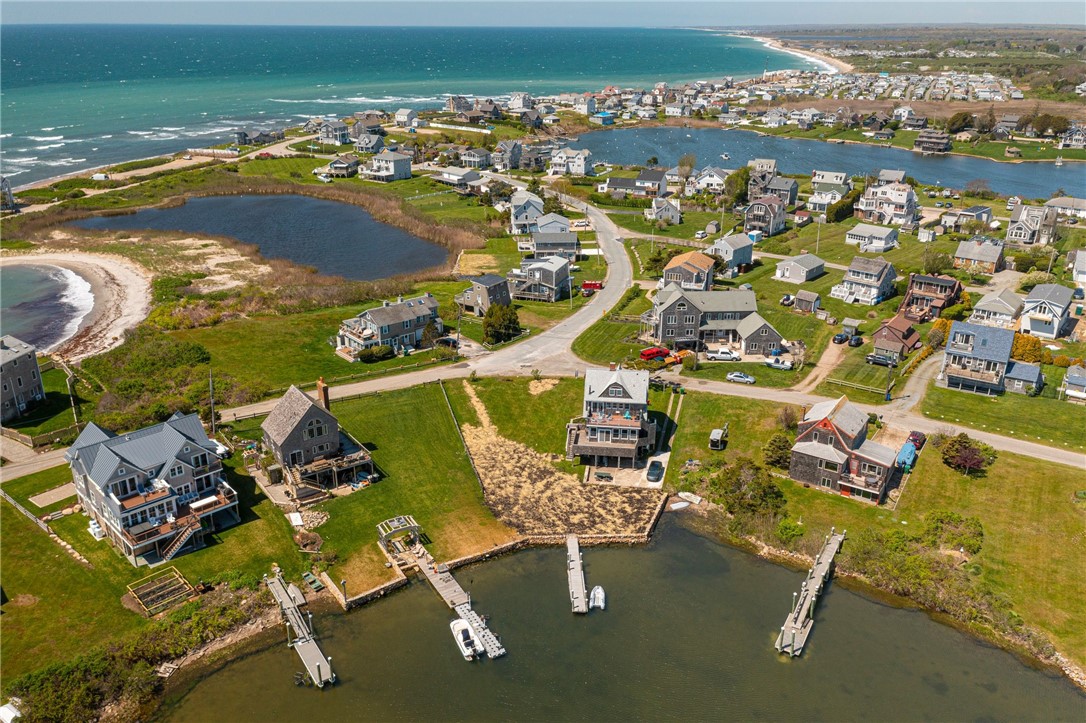Aerial view of coastal homes and docks beside an inlet, with ocean and beach beyond.