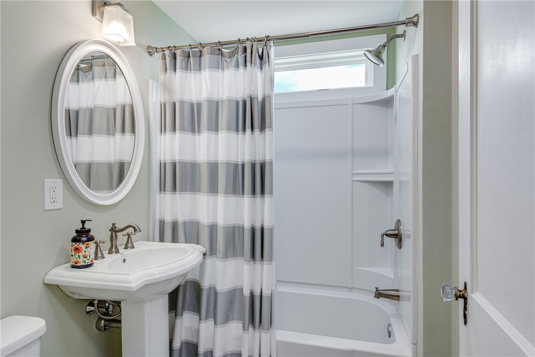 Bathroom with pedestal sink, oval mirror, and tub-shower behind a gray-and-white striped curtain.