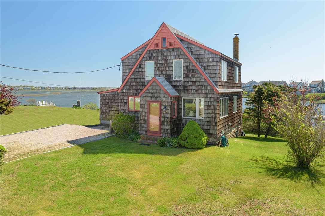 Shingle-sided waterfront house with red trim, a steep gabled roof, and a broad green lawn.