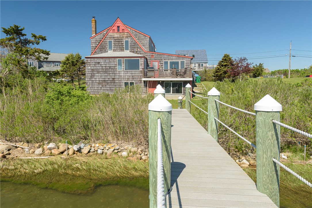 Shingle-style coastal home with coral-red trim and a boardwalk crossing marsh grass and water.