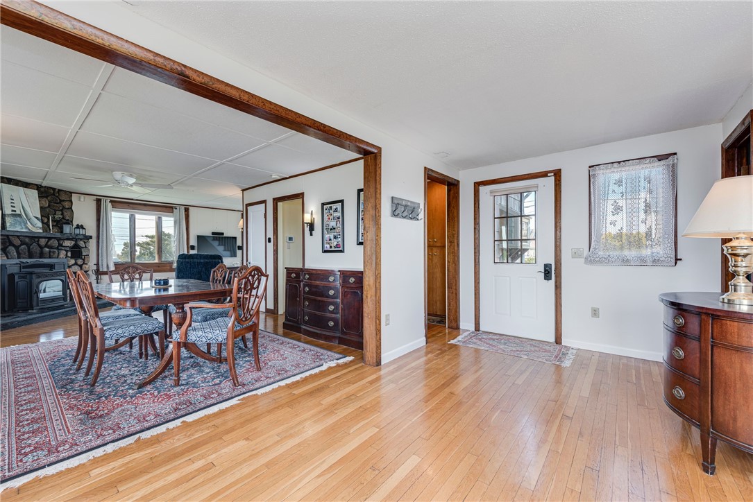 Dining room with a wood table and chairs beside a stone fireplace and hardwood-floored entryway.