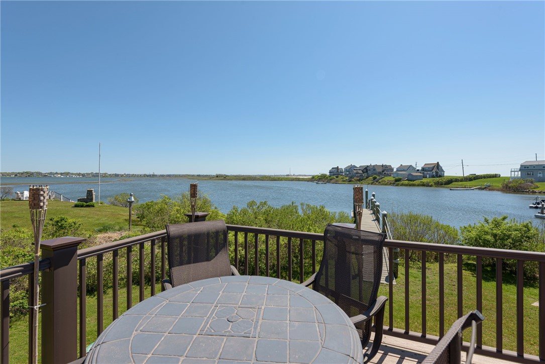 Deck with patio table and chairs overlooking an inlet and distant waterfront homes.