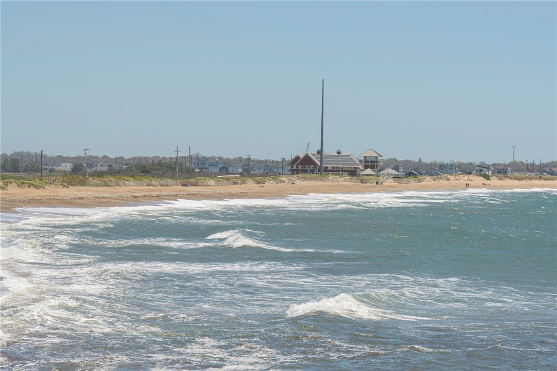 Ocean waves roll toward a sandy beach lined with coastal buildings.