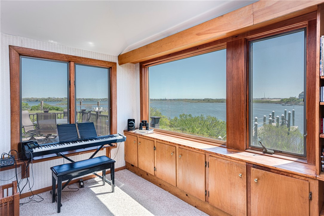 Wood-trimmed room with a digital piano and wide windows overlooking the water.