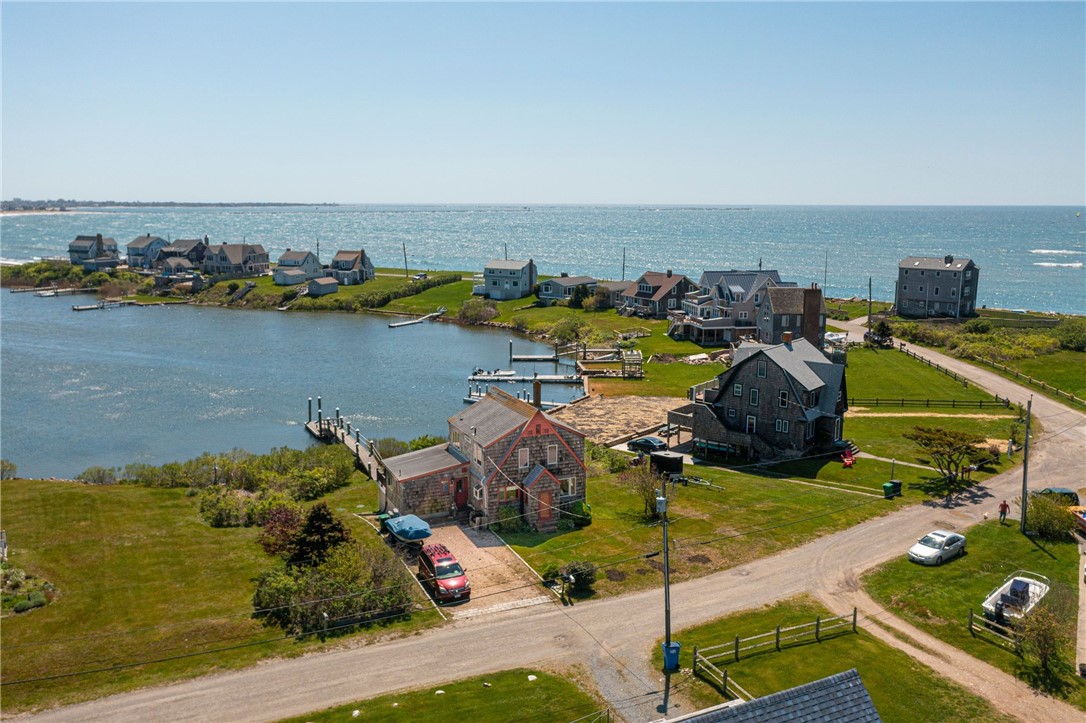 Aerial view of a shingled waterfront home beside an inlet and private dock, with the ocean beyond.