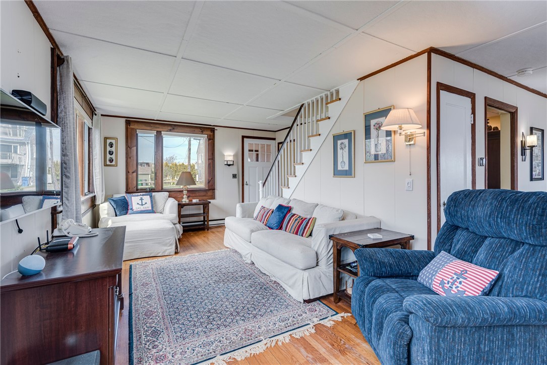 Living room with white sofas, a blue recliner, and a staircase beside large windows.