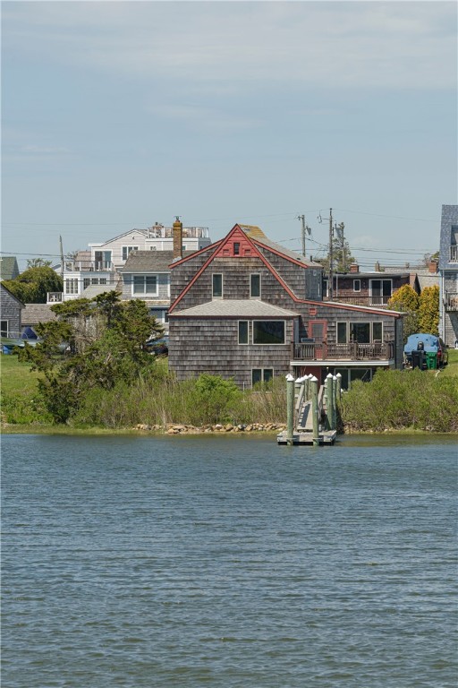 Shingled coastal house with red trim across the water, with a small dock in front.