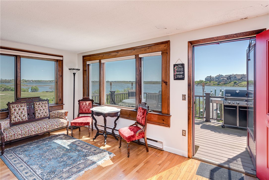 Living room with wood-trimmed windows overlooking the water and an open door to a deck with a grill.