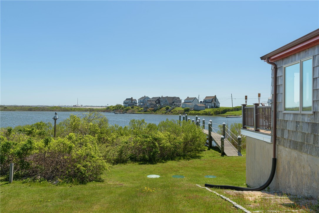 Waterfront yard with a wooden dock, water views, and part of a shingled home.