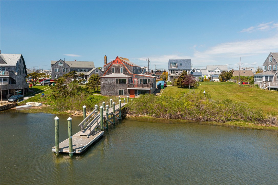 Waterfront shingle-sided home with orange trim, private dock, and a broad lawn beside the water.