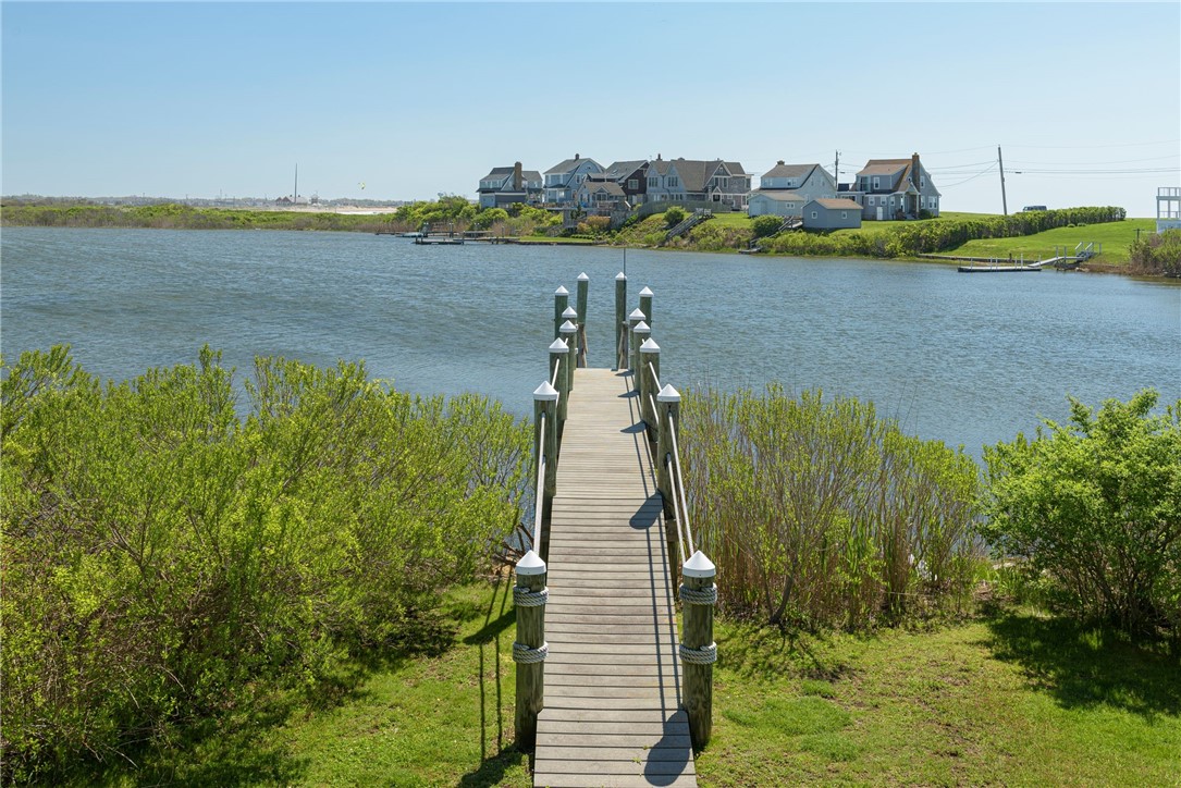 A wooden dock reaches into an inlet, with waterfront homes across the water.