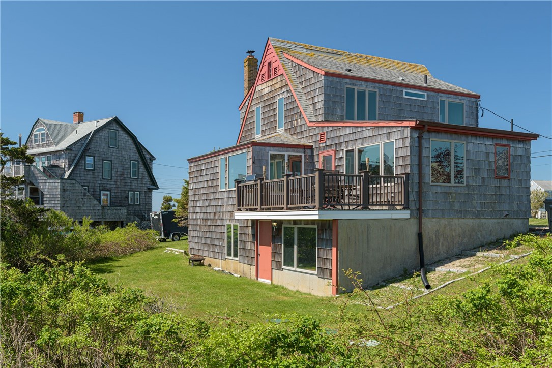 Cedar-shingle coastal home with coral-red trim and a second-floor deck.