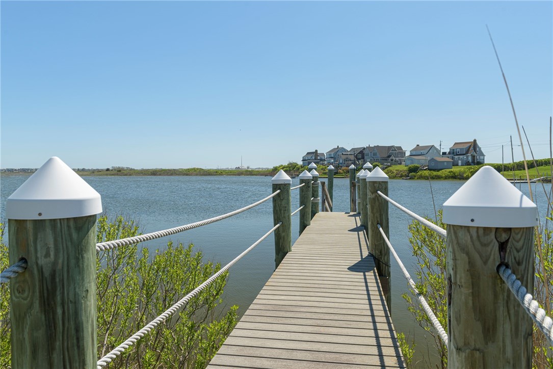 Wooden dock extends across calm water toward houses along a green shoreline.