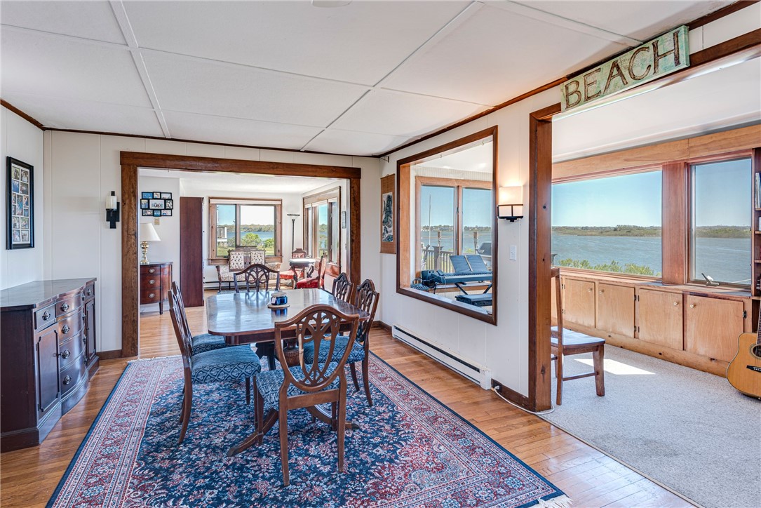 Dining room with a patterned rug and dark wood trim, opening to a sunroom overlooking the water.