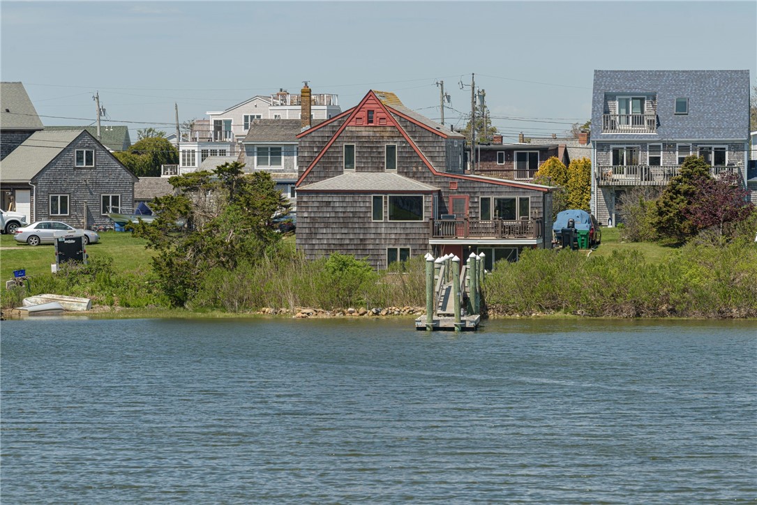 Shingled waterfront house with red trim and a small dock extending into the water.