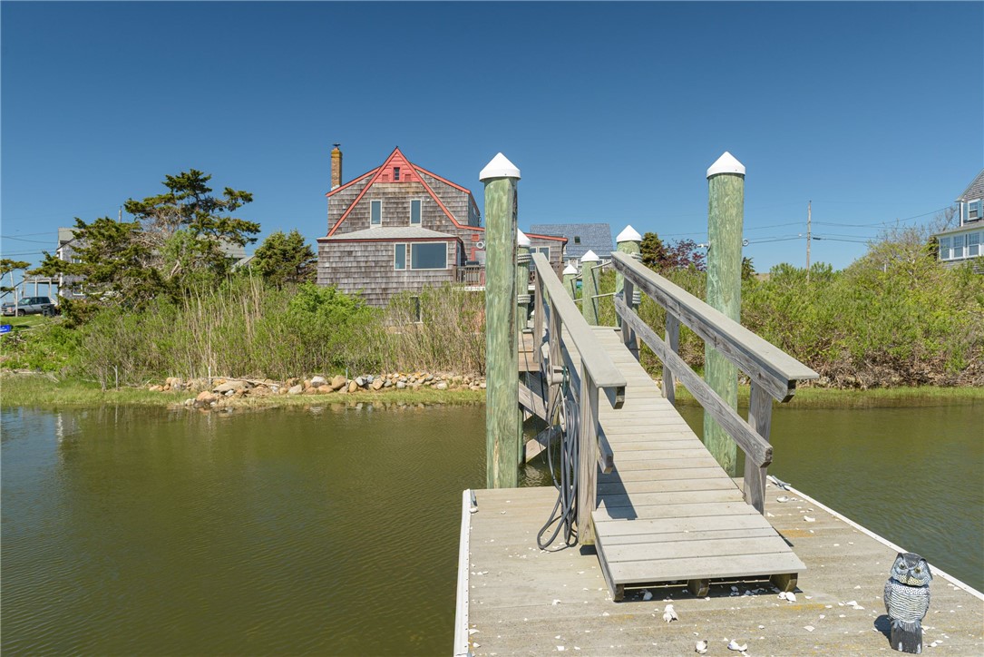 Wooden dock and gangway lead from the water toward a shingle-style waterfront house.