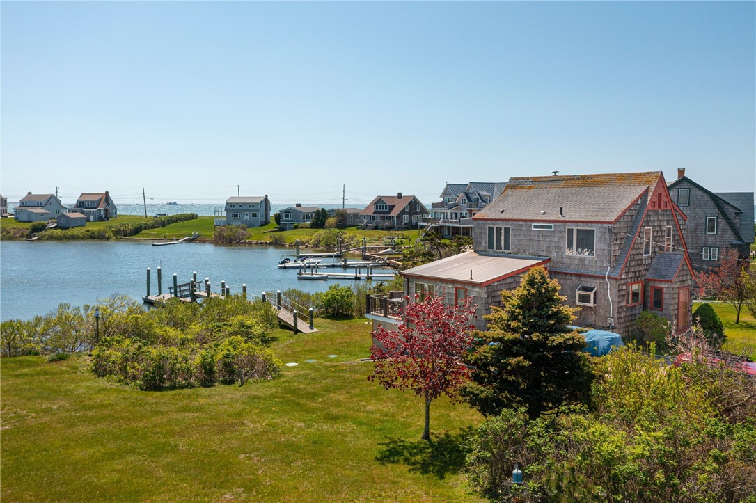 Shingle-sided coastal home beside an inlet, with a lawn, private dock, and neighboring waterfront houses.