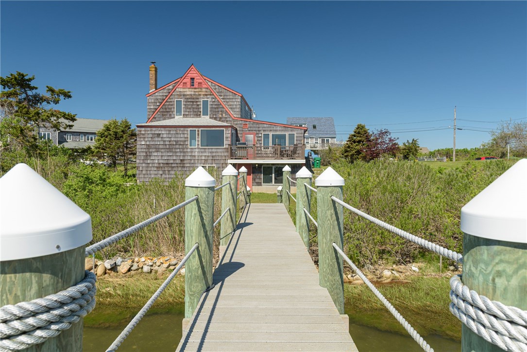 Coastal shingle-style home at the end of a rope-railed boardwalk over marsh water.