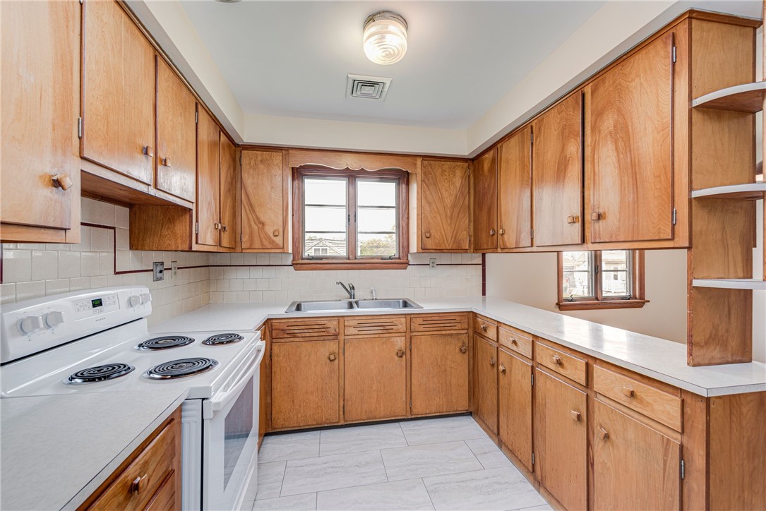 Kitchen with honey-colored wood cabinets, white countertops, and a white electric range.