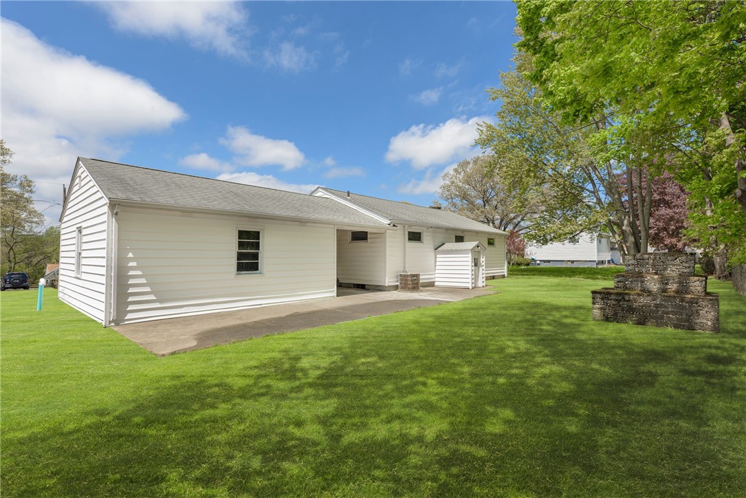 Rear and side of a white-sided home beside a broad lawn, mature trees, and a tiered stone planter.