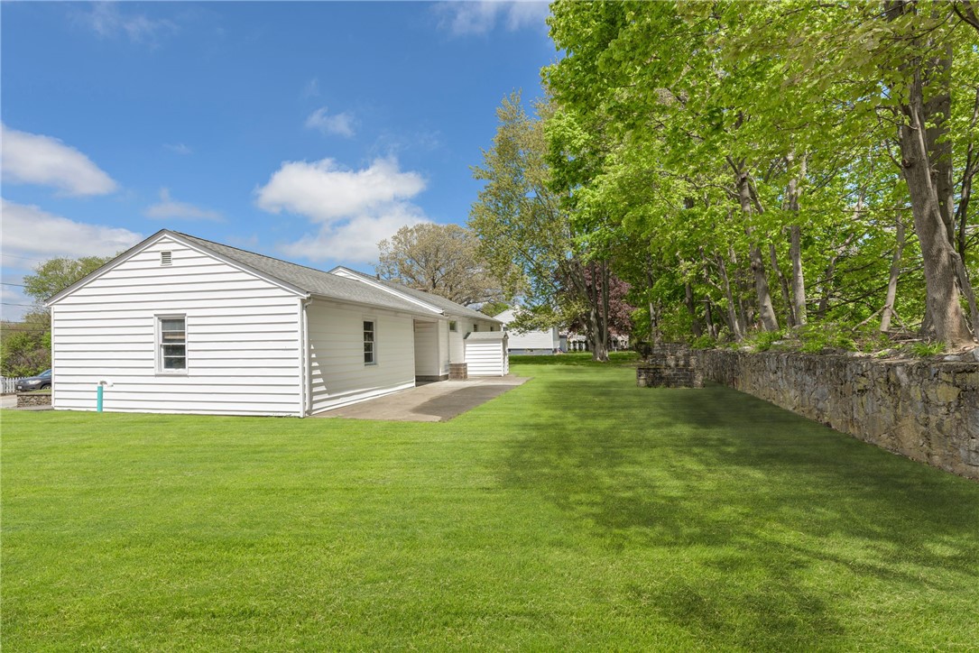 White single-story house beside a broad lawn and stone wall under mature trees.