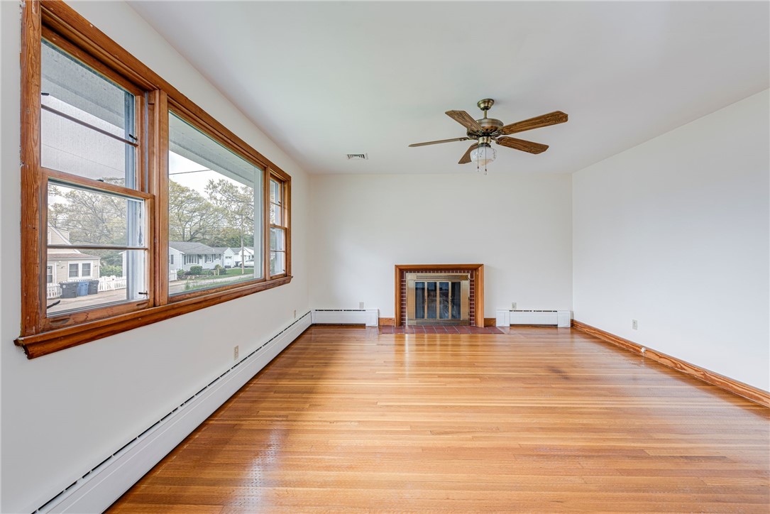 Empty living room with hardwood floors, large wood-trimmed windows, and a brick fireplace.