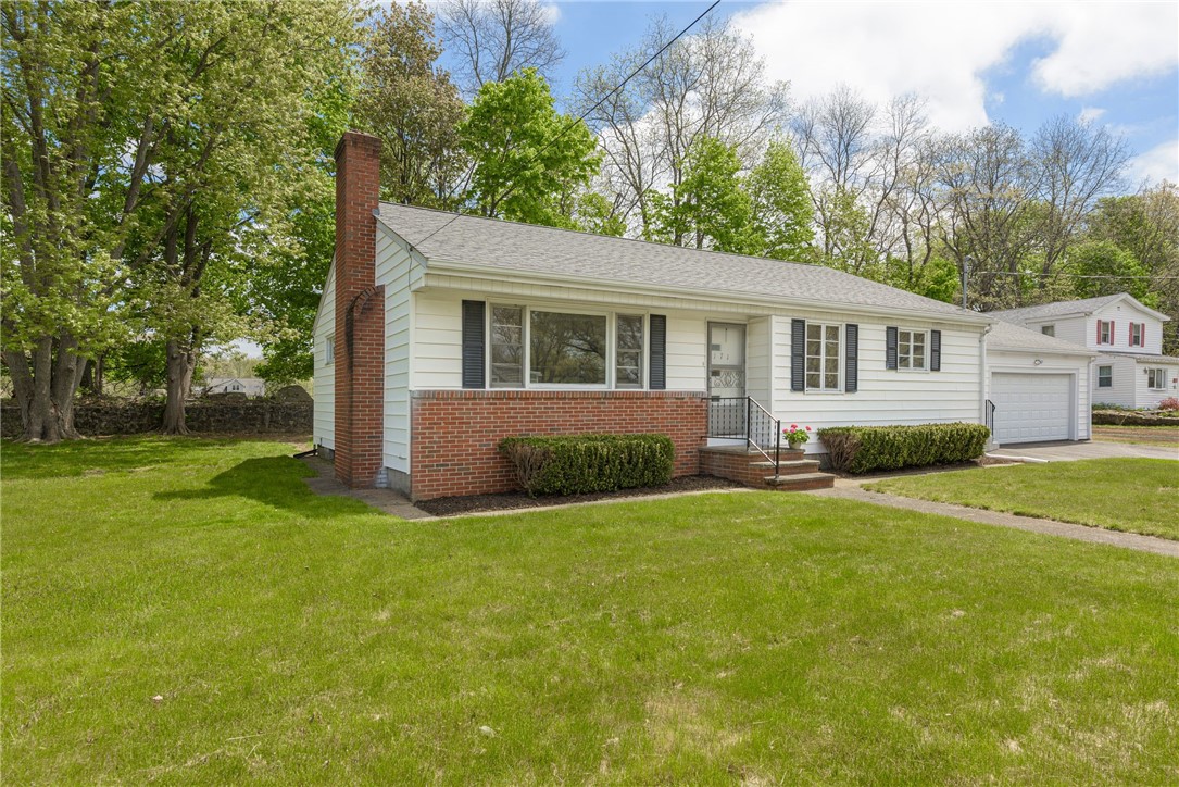 White ranch house with a brick facade, tall chimney, attached garage, and broad green lawn.