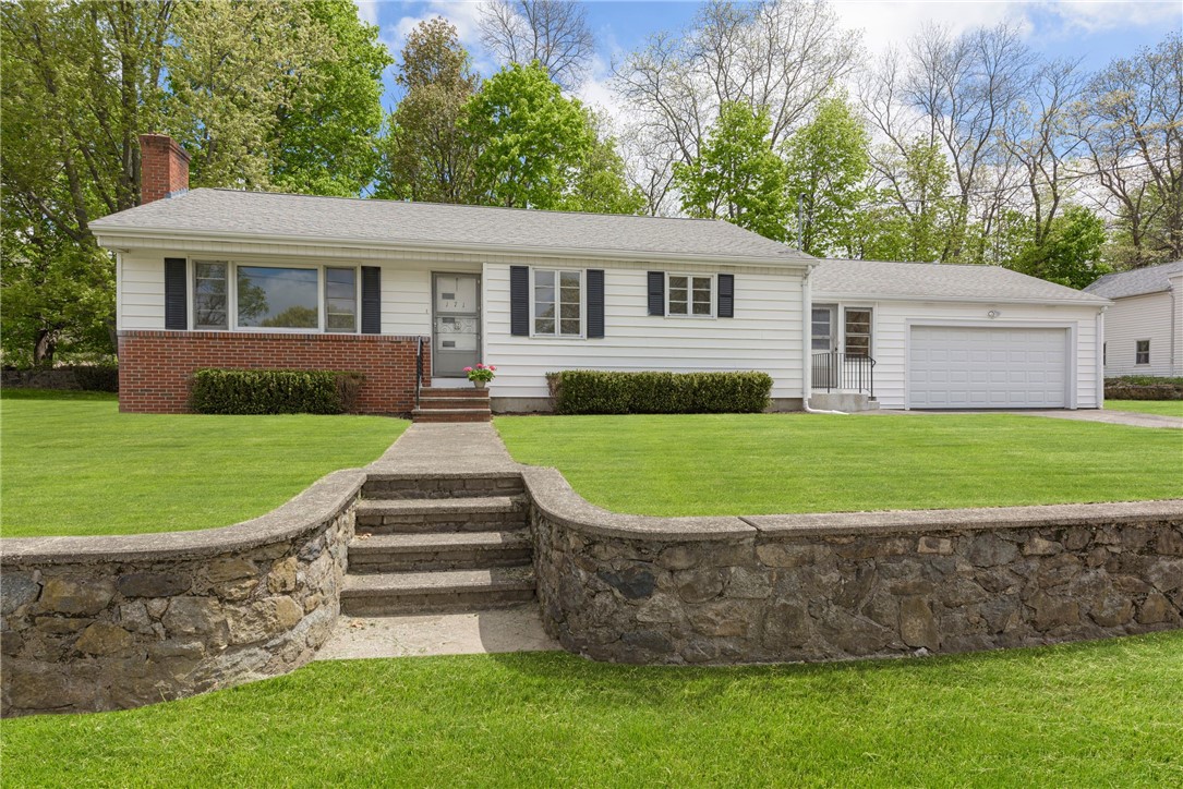 White ranch house with an attached garage, front lawn, and stone retaining wall and steps.