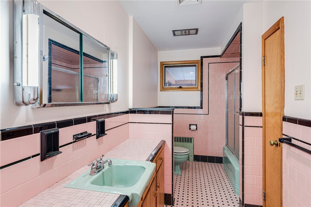 Vintage bathroom with pink tile, black trim, mint-green sink, and glass-enclosed shower.