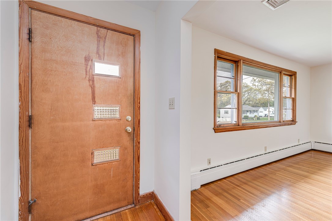 Empty entryway and room with a weathered wooden front door, hardwood floors, and a wide window.