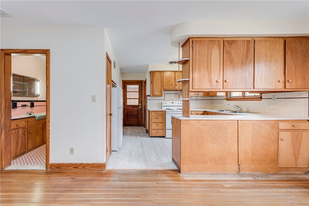 Kitchen with honey-toned wood cabinets and a peninsula; adjoining bathroom visible through the doorway.