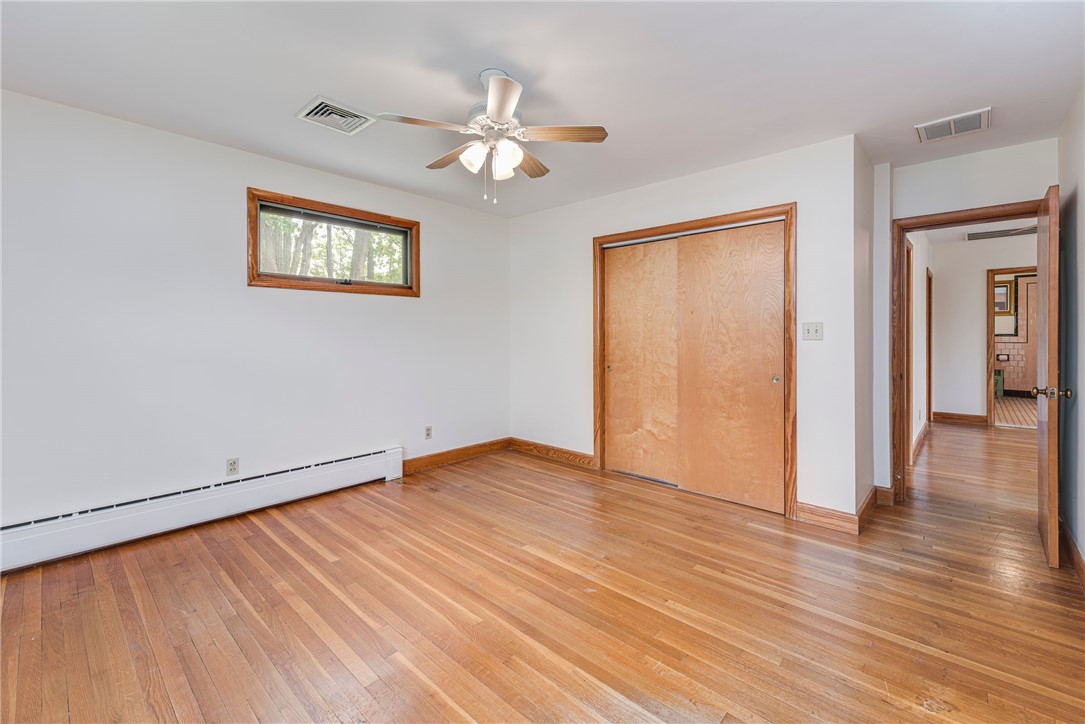Vacant bedroom with hardwood floors, sliding wooden closet doors, and a ceiling fan.