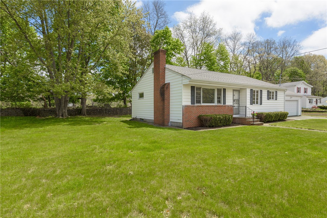 Single-story white ranch house with a brick chimney, attached garage, and broad green lawn.