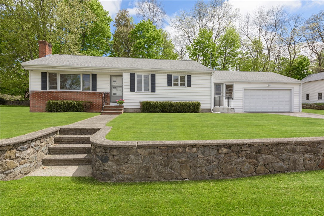 White ranch house with attached garage, brick facade, and stone retaining wall along the front lawn.