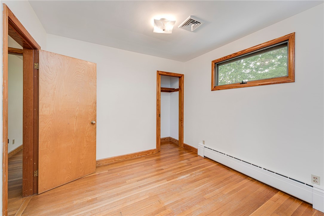 Empty bedroom with hardwood floors, wood trim, a small closet, and a high horizontal window.